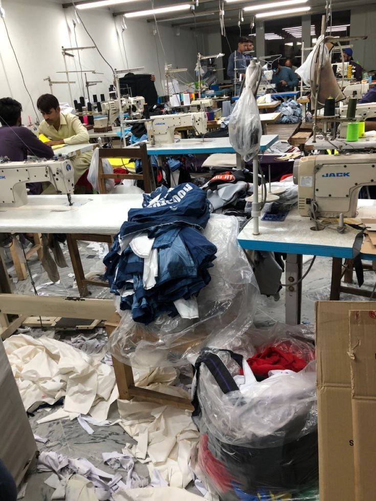 Workers at industrial sewing machines with stacks of stitched garments on the factory floor